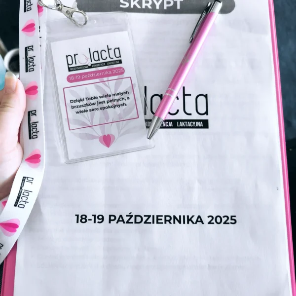 Zbliżenie na materiały konferencyjne leżące na różowej podkładce z klipem. Widoczny jest identyfikator z logo "prolacta" i napisem "Dzięki Tobie wiele małych brzuszków jest pełnych, a wiele serc spokojnych", różowy długopis oraz dokument z nagłówkiem "SKRYPT" i datą "18-19 PAŹDZIERNIKA 2025".